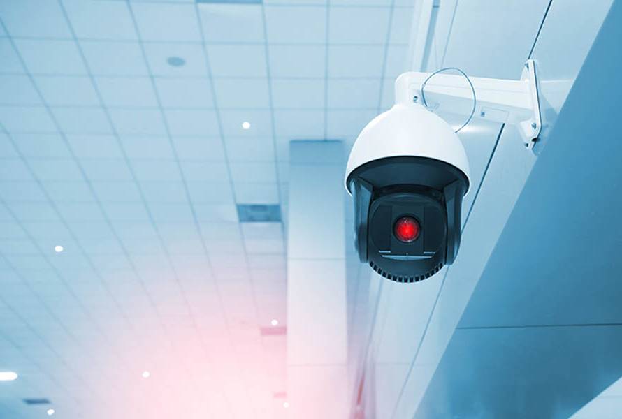 How Custom Surveillance Systems Can Secure Your Property 24/7; Modern CCTV camera on a wall. A blurred night cityscape background. Concept of surveillance and monitoring.